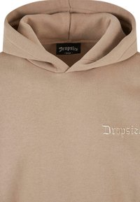 Beige Kapuzenpullover mit weicher Textur, ausgestattet mit einer verstellbaren Kapuze und dem gestickten "Dropsize"-Logo in Weiß auf der linken Seite.