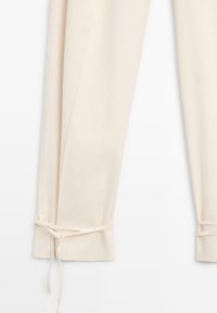Hose in Cremefarbe mit Schnürung am Knöchel, geradem Bein und glatter Stoffstruktur.