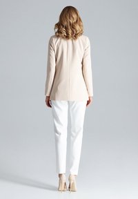 Beige op maat gemaakte blazer, witte aansluitende broek en beige hoge hakken. Glad materiaal met lange mouwen en een minimalistisch ontwerp.