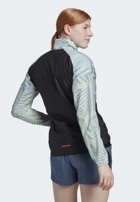 Schwarze Jacke mit hellblauen gemusterten Ärmeln, mit Stehkragen und elastischen Bündchen. Enthält einen kleinen orangefarbenen Akzent am Saum.