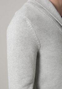 Světlounce šedý pletený svetr s texturovaným vzorem, s ohrnutým límcem a hladkými rukávy, zdůrazňující měkkou tkaninu a jednoduchý design.