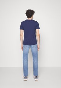 Camiseta de algodón azul marino con cuello redondo, combinada con vaqueros rectos de color azul claro. Los zapatos son predominantemente blancos con detalles oscuros.