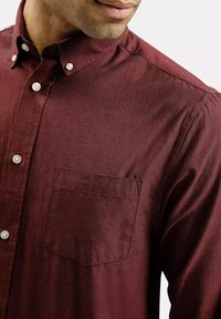 Burgundowa koszula zapinana na guziki z kołnierzykiem, długimi rękawami, kieszenią na piersi oraz gładką teksturą z kontrastującymi białymi guzikami.