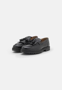 Mocassins en cuir noir avec un devant à franges, une finition lisse et une semelle en caoutchouc épaisse avec des rainures de traction.