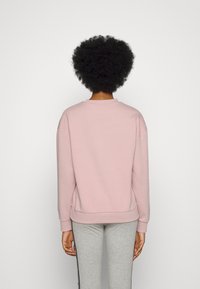 Helle rosa Sweatshirt aus weichem, strukturiertem Stoff mit rundem Hals, gerippten Manschetten und lockerer Passform, kombiniert mit grauen Sweatpants.