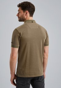 Khaki polo skjorte med krave, korte ærmer og subtil struktur. Har et lille logo-mærke på bagsiden og en lige kant.