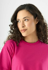 Heldroze katoenen T-shirt met een ronde hals, voorzien van een klein geborduurd logo op de borst en korte mouwen. Gladde textuur.