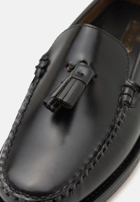 Sorte skinnloafere med en glatt overflate, dekorative duskdetaljer og håndsydde accenter langs kanten. Klassisk design.