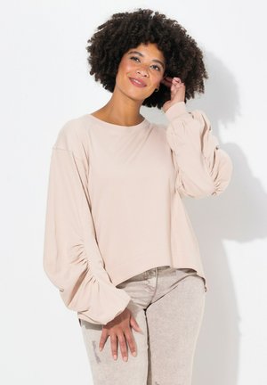 Lichtroze shirt met lange mouwen, voorzien van geplooide pofmouwen en een ronde zoom. Zachte stof met een comfortabele pasvorm. Gdrag met lichte broek.