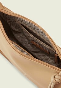Tan leren tas met een ritssluiting aan de bovenkant, voorzien van een voering met een vissengraatpatroon en een klein binnenzakje. Knoopdetail aan de zijkant.