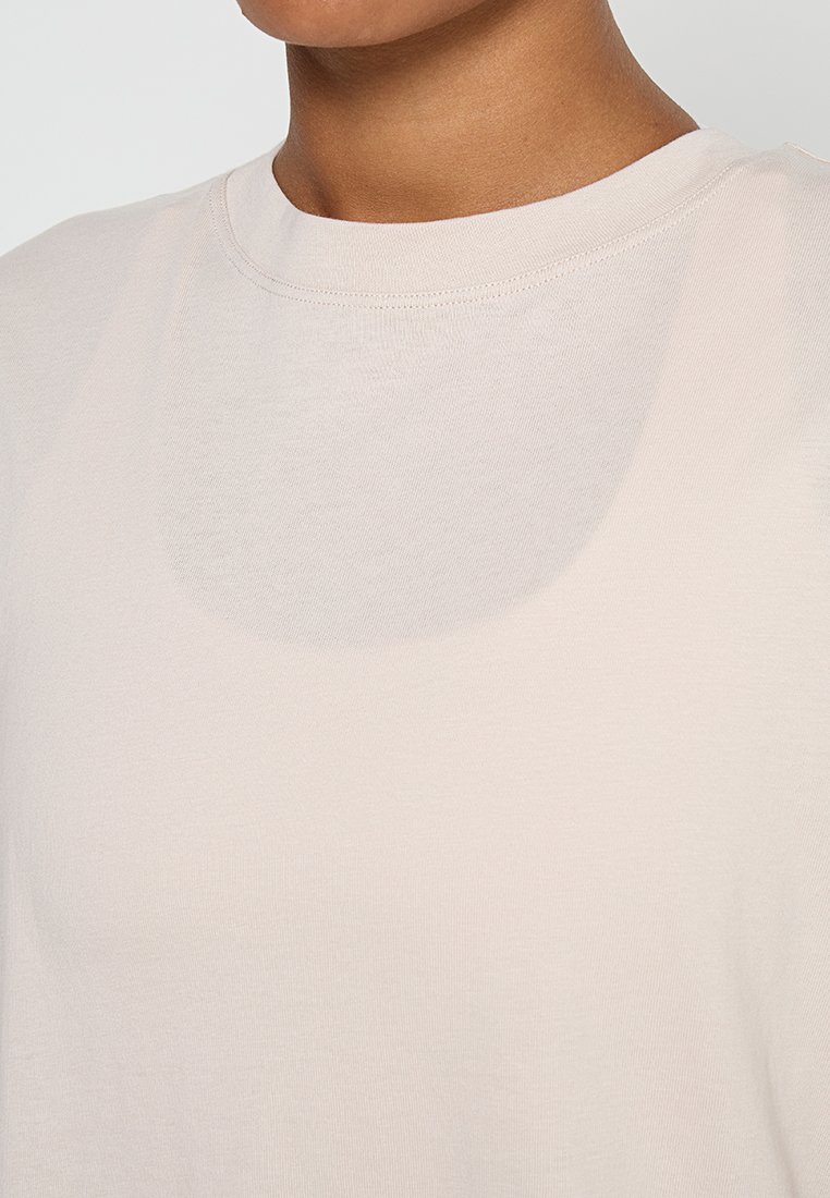 Nahaufnahme einer Person, die ein leicht beiges Rundhals-T-Shirt trägt, das die Stoffstruktur und die Details des Halsausschnitts zeigt.