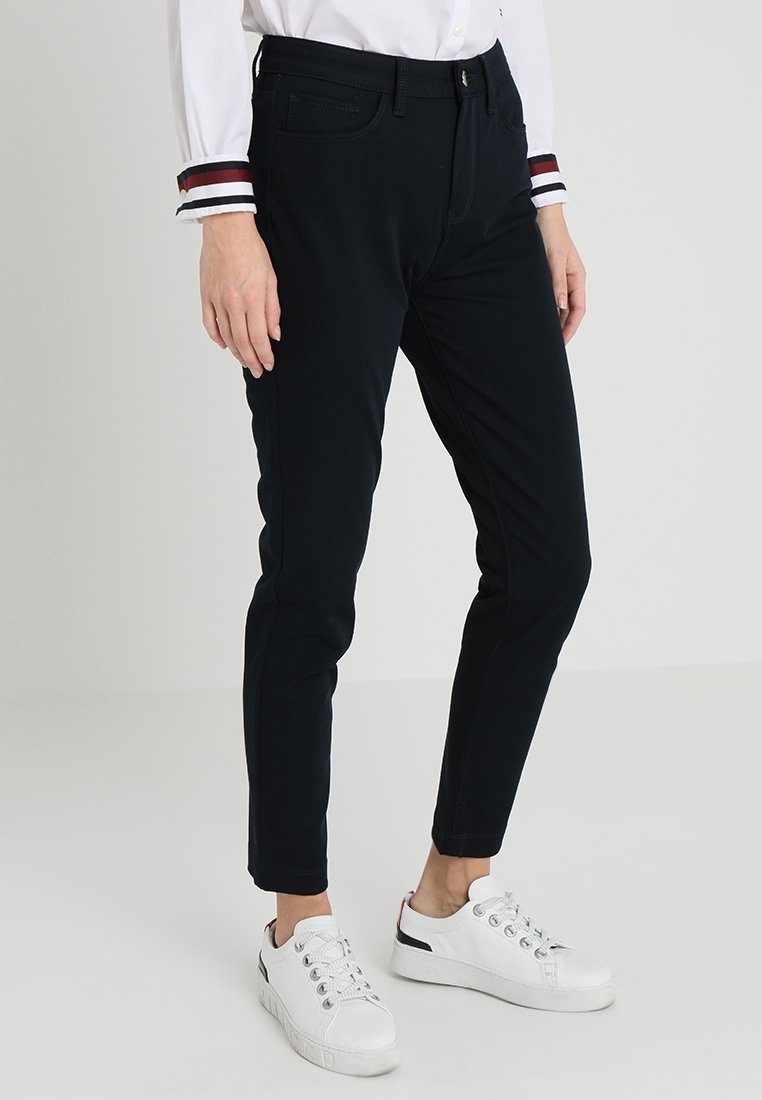 Marina stretchbyxor med slim fit, som har sidofickor och gylf med dragkedja. Kombinerad med vita lågskor och en vit skjorta med randiga detaljer.