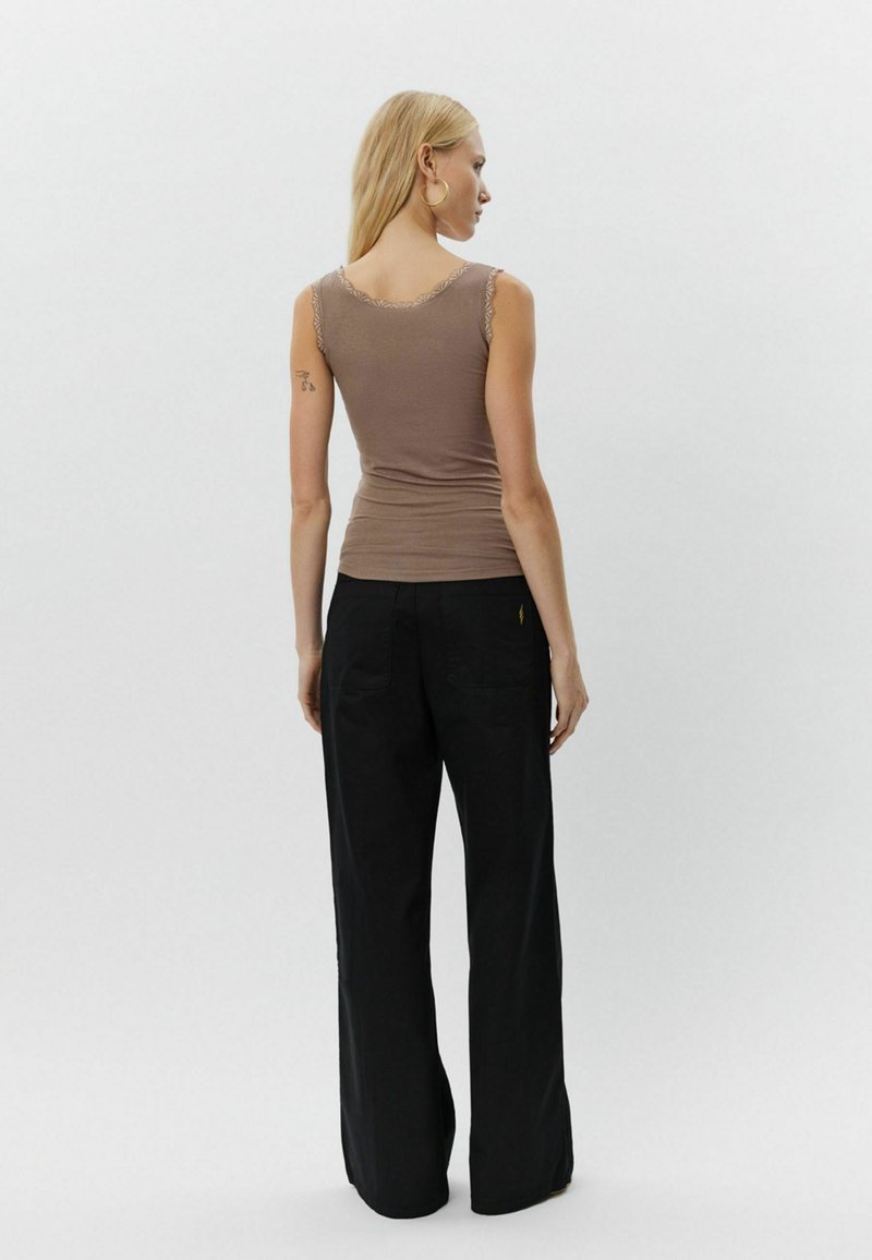 Barna pántnélküli felső csipkés díszítéssel a vállaknál, laza fekete nadrággal párosítva. Főbb jellemzői a karcsú szabás és a puha anyag.