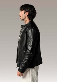 Veste en cuir noir avec une texture lisse, fermeture éclair à l'avant, poches latérales et design ajusté, présentée portée sur une chemise à motifs.