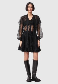 Haut en dentelle noire avec manches transparentes superposé à une jupe noire à volants. Associé à des bottes en cuir noires montantes jusqu'aux genoux.