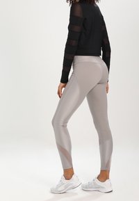 Harmaat leggingsit, joissa on teksturoitu kuvio, yhdistetty mustaan läpinäkyvään pitkähihaiseen paitaan. Valkoiset urheilukengät täydentävät asua.