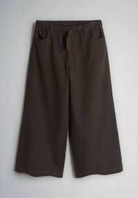 Tumši brūnas plaša griezuma bikses ar elastīgu jostu un auklu, ar priekšējām kabatām, redzamas pret vienkrāsainu pelēku fonu.