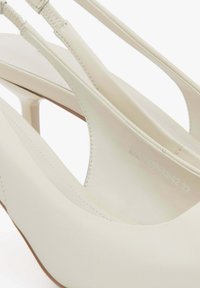 Białe skórzane czółenka na słupku z eleganckim wzornictwem, spiczastym noskiem i smukłym wysokim obcasem. Posiadają przeszyte detale i gładką teksturę.