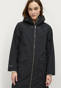 Veste noire imperméable avec fermeture éclair à l'avant, capuche ajustable, deux poches avant et coutures ton sur ton. Présente un logo sur la manche.