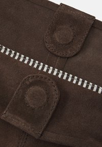 Pruun suede kangas, millel on tikkimise detailid ja kaks ringikujulist nupuvajutust. Valge ja pruuni triibuline vooder on nähtav zippaaugu ääres.