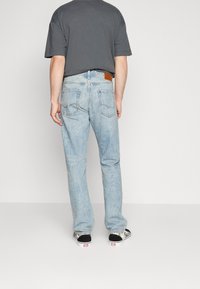 Vaaleansiniset farkut suoralla leikkauksella, joissa on takataskut ja ruskea nahkainen logopatchi vyötäröllä. Yhdistetty mustiin ja hopeisiin kenkiin.