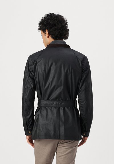 Veste noire imperméable avec un col marron, taille ceinturée et détails aux épaules ; présente une texture lisse et une coupe ajustée.