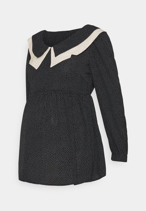 Robe noire à manches longues avec petits pois blancs et grand col blanc pointu contrasté avec des pois noirs.