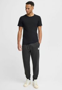 Sort kortærmet t-shirt parret med mørkegrå sweatpants, der har snor i taljen og et lille logo-patch, båret med lyse sneakers.