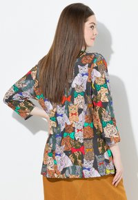 Multicolored blouse featuring a cat print with various patterns and colors. Three-quarter sleeves, lightweight fabric, and a relaxed fit.