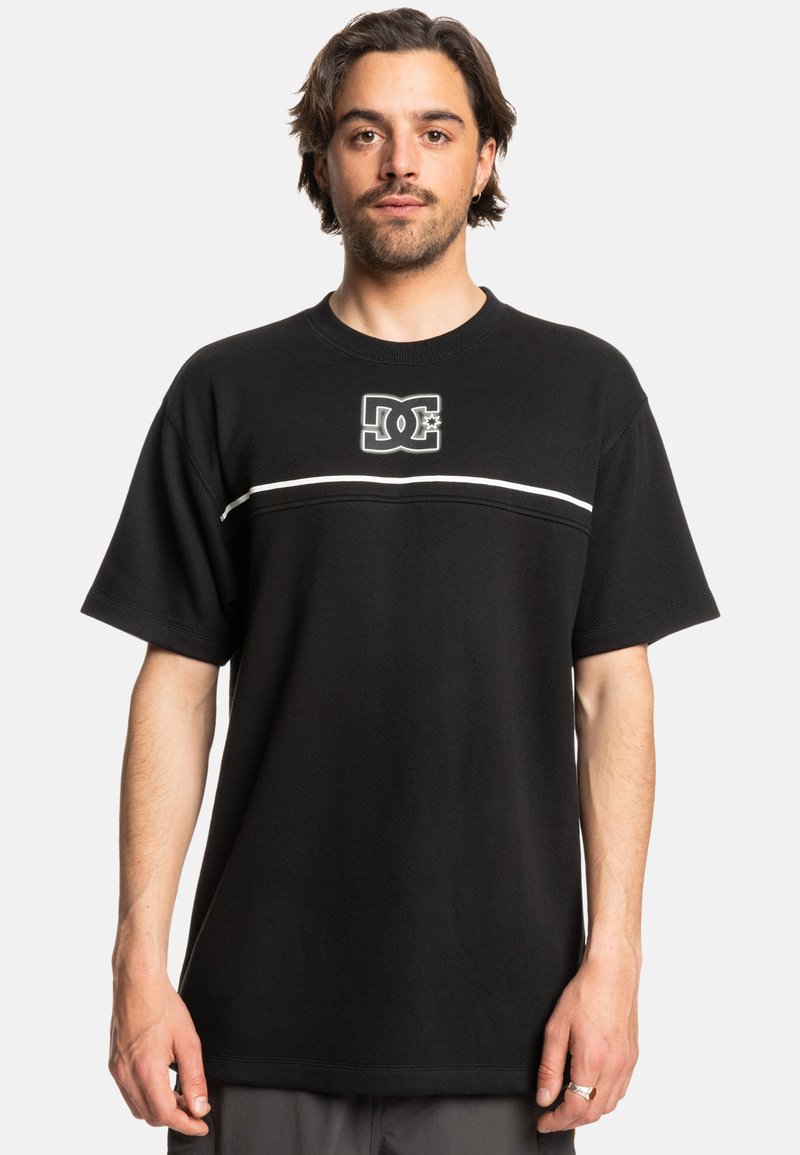Black short-sleeve t-shirt made of cotton blend, featuring a white horizontal stripe and DC logo in the center. Loose fit with ribbed neckline.