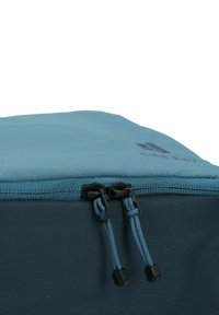 Bolsa con cremallera de color teal, hecha de tejido texturizado, con tiradores de cremallera dobles y un logo en el lateral. Forma rectangular compacta.