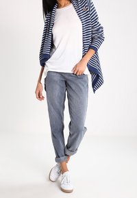 Cardigan a righe blu e bianche sopra una maglietta bianca semplice, abbinato a jeans blu chiaro arrotolati e sneakers bianche con dettagli verdi.