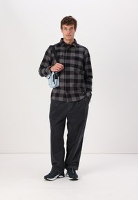 Checkered black and gray flannel shirt, loose black corduroy pants, and navy sneakers. Small light blue crossbody bag with zipper.