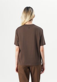 Tricou scurt din bumbac de culoare maro, cu mâneci scurte, având un guler rotund și un detaliu cu logo mic în spate, aproape de guler.