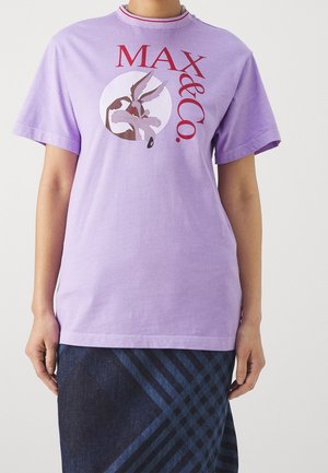 Person trägt ein lavendelfarbenes T-Shirt mit einem Cartoon-Kojotengesicht und rotem "MAX & CO." Text, kombiniert mit einem dunkelblauen karierten Rock.