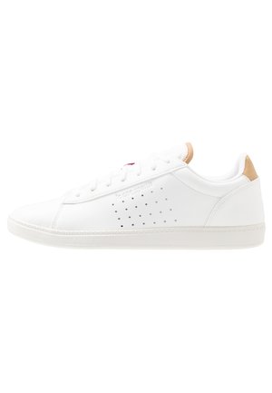 Biały niski sneaker z perforowanym wzorem po bokach, białymi sznurowadłami i beżowymi akcentami na języku i pięcie.