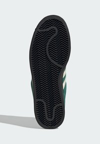 Groene sneakerzool met een gestructureerd, zwart rubberen ontwerp met een golvend patroon. Opvallende groeven verbeteren de grip en tractie.