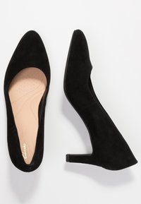 Chaussures à talons hauts en daim noir avec un bout pointu et un petit talon carré. L'intérieur présente une semelle rembourrée couleur beige clair avec des perforations.