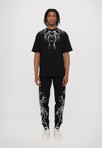 T-shirt nera con grafica di un fulmine e testo "PHOBIA", abbinata a pantaloni jogger neri con design a striscia di fulmine, indossata con sneakers bianche.