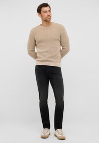 Suéter de punto beige con cuello redondo, combinado con jeans oscuros de corte ajustado y zapatillas beige con acentos en blanco. Tejido texturizado en azul.