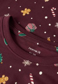 Red cotton t-shirt with a crew neck featuring a festive print of candy canes, gingerbread men, gift boxes, and snowflakes on a dotted background.