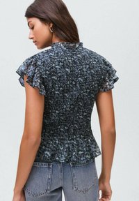 Blusa blu a fantasia con maniche corte a volant, vita arricciata e orlo peplum, abbinata a jeans in denim a vita alta.