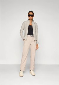 Gaiši pelēka rāvējslēdzēja jaka virs melnas virsdrēbes, bēša krāsas bikses ar kabatām un gaišas sporta kurpes. Modelis valkā lielizmēra saulesbrilles.