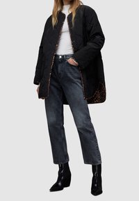 Pikowana czarna kurtka z podszewką w panterkę, zestawiona z wysokim stanem ciemnoszarymi dżinsami i błyszczącymi czarnymi botkami.