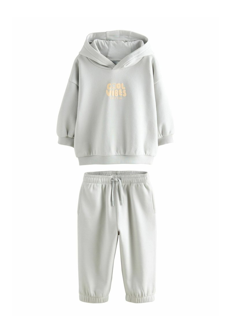 Hellgrauer Hoodie und Jogger-Set aus weichem Material. Der Hoodie hat einen Frontgrafik mit dem Text "Cool Vibes" in hellem Beige. Elastische Bündchen.
