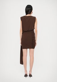 Pruun kortsutega kleit asümmeetrilise äärega, varrukateta disainiga ja sileda tekstuuriga. Ühel küljel on drapeeritud kangaste detail.