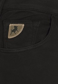 Jeans de mezclilla negra con un parche de bolsillo triangular que presenta la silueta de un toro, resaltado por costuras en contraste a lo largo del borde.