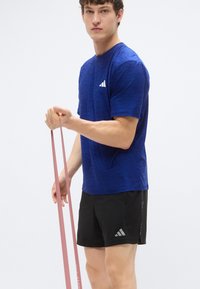 Modré štruktúrované športové tričko s malým bielym logom, v kombinácii s čiernymi šortkami s akcentovaným logom, držiace ružový odporový pás.