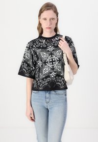 Svart-hvitt mønstret oversized t-skjorte med korte ermer, med paisley-design, kombinert med lyseblå jeans og en liten hvit veske.