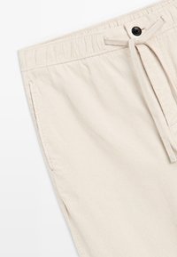 Beige corduroy shorts with an elastic waistband, drawstring tie, and a single black button detail at the front. Textured fabric, casual design.